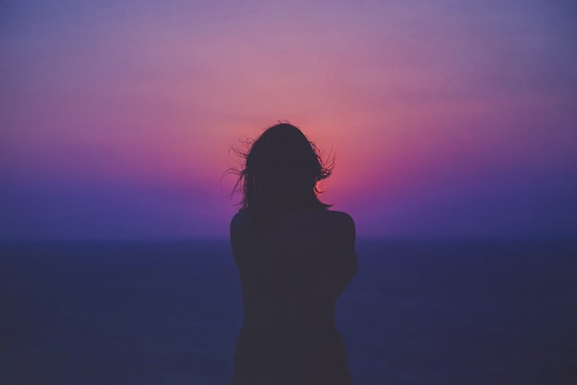 silhouette of woman standing against dark pink sunset sky