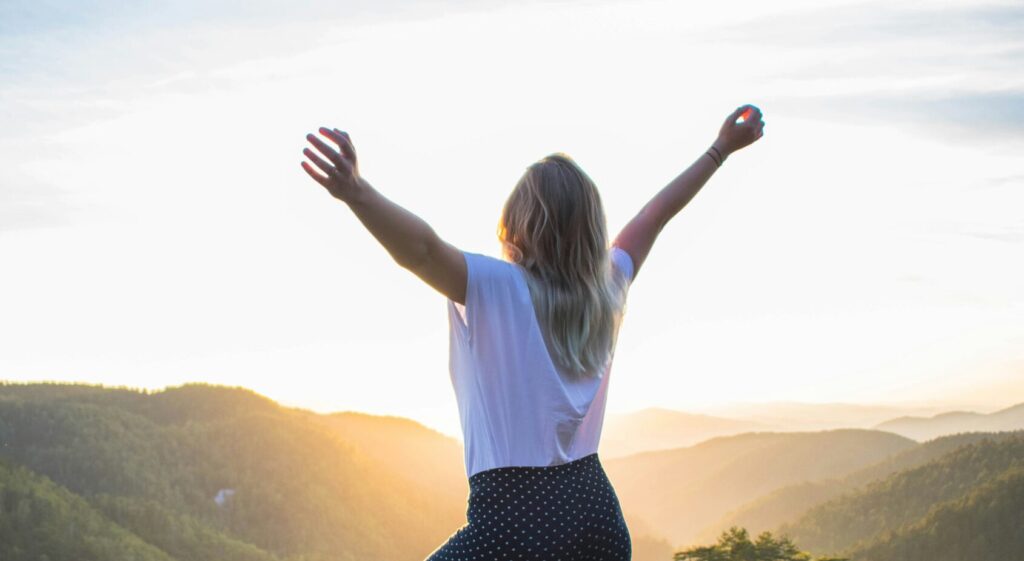 Woman holding her hands above head with mountains in the background