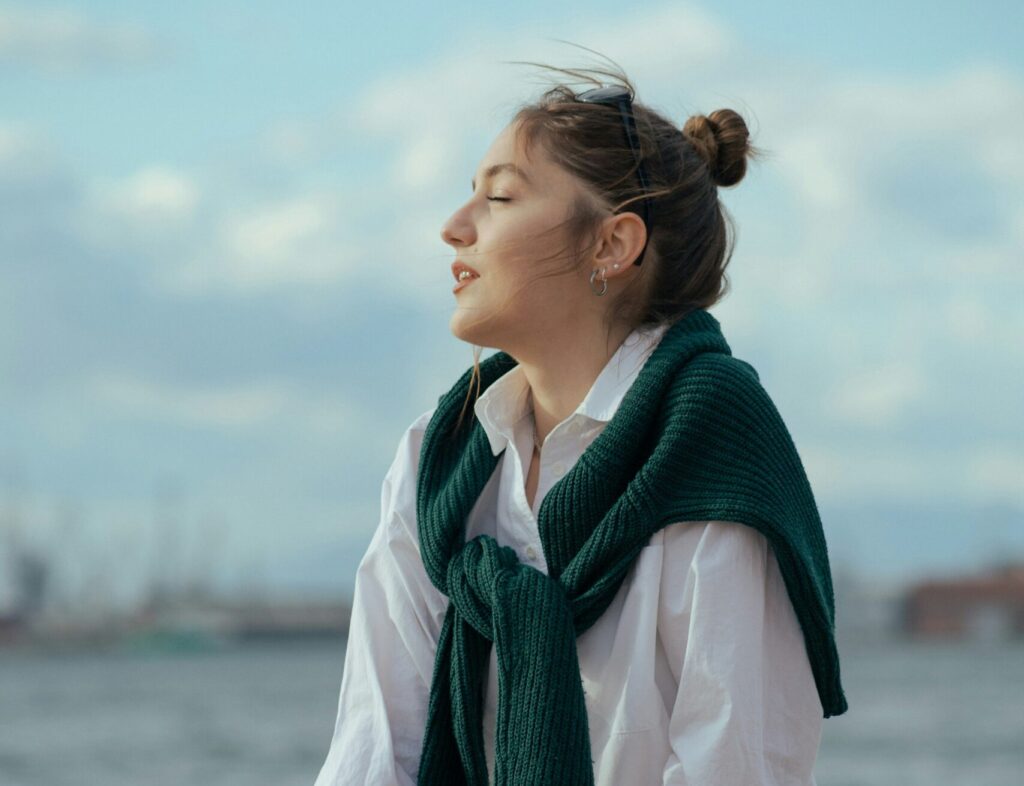 Woman in white shirt with green sweater around her shoulders looking toward the sky with her eyes closed, looking relaxed after depression therapy.