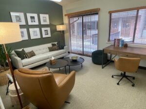 Denver therapy office with two brown leather chairs, light grey couch in front of green wall with gallery of six white picture frames