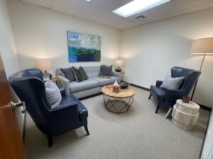 Denver therapy office with two blue wing back chairs and a grey couch in front of a white wall with a blue painting